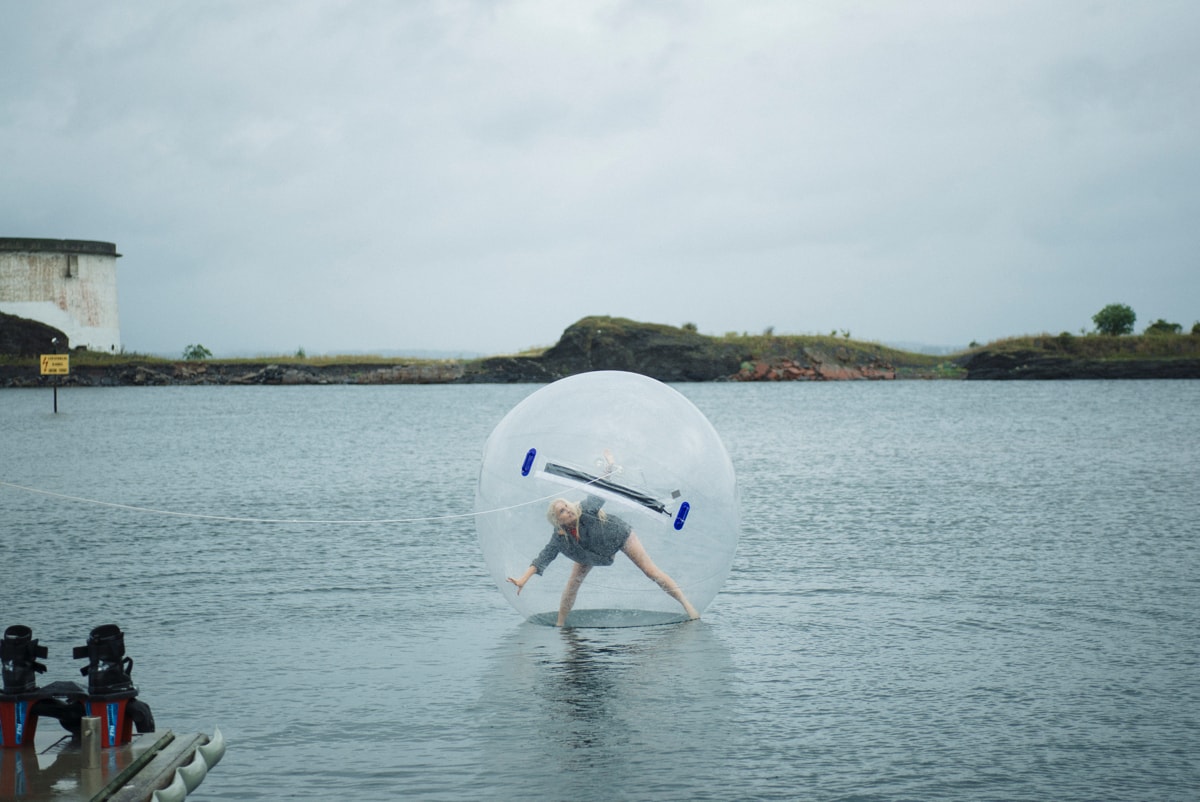 Girl inside a plastic bubble filled with air, walking on water.